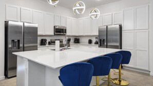 A modern kitchen with white cabinets, stainless steel appliances, a central island with blue bar stools, and pendant lighting. - Family-friendly Luxury Home Near Disney & More (Kissimmee)