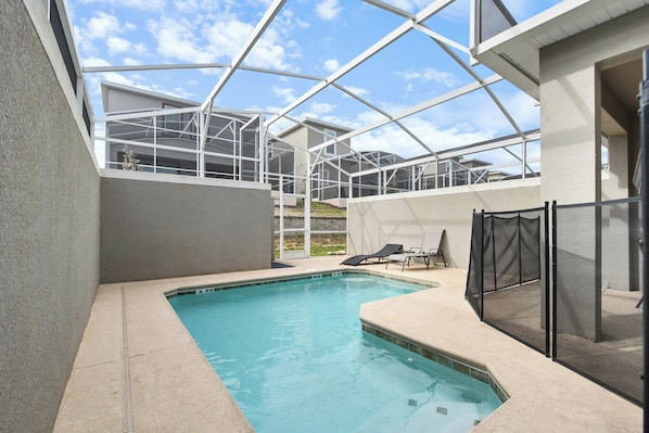 A swimming pool with a glass enclosure, surrounded by a concrete deck and a covered seating area.