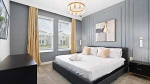 A modern bedroom with a large bed, grey walls, a chandelier, and a view of the outside. - Champions Gate 6BR Private Theater Games Pool Spa (Kissimmee)