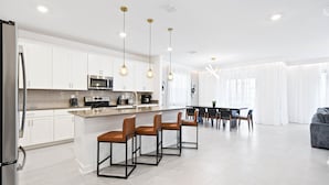 A modern kitchen with white cabinets, stainless steel appliances, and a central island with bar stools. - Champions Gate 6BR Private Theater Games Pool Spa (Kissimmee)