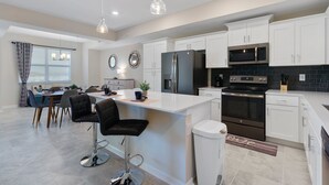 A modern kitchen with white cabinets, a black refrigerator, stainless steel appliances, and a bar area with stools. - Storey Lake Sweet 2br Home 3121 (Kissimmee)