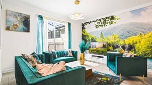 Ein Wohnzimmer mit türkisfarbenen Sofas, einem Flachbildfernseher und einem Wandgemälde einer Waldlandschaft.