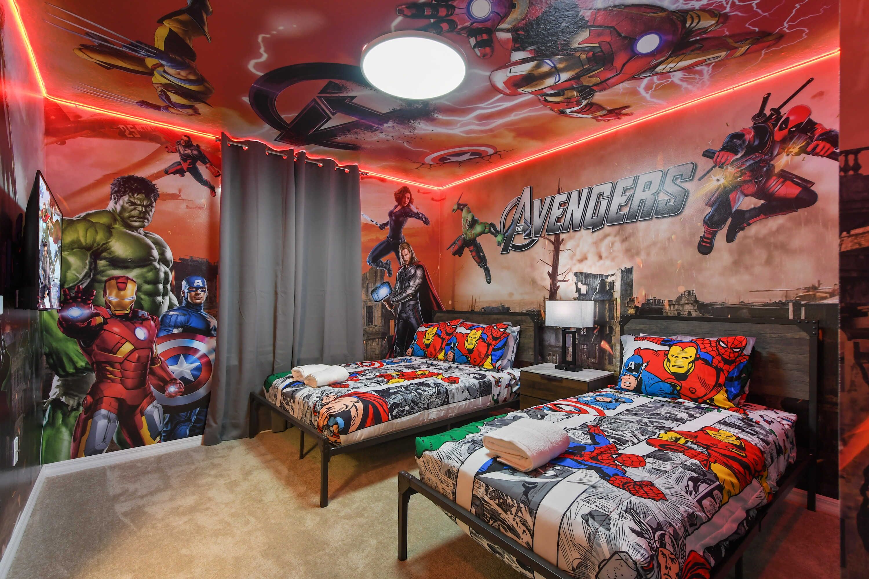 A room with two beds, each with superhero-themed bedding and a mural of Avengers characters on the wall.