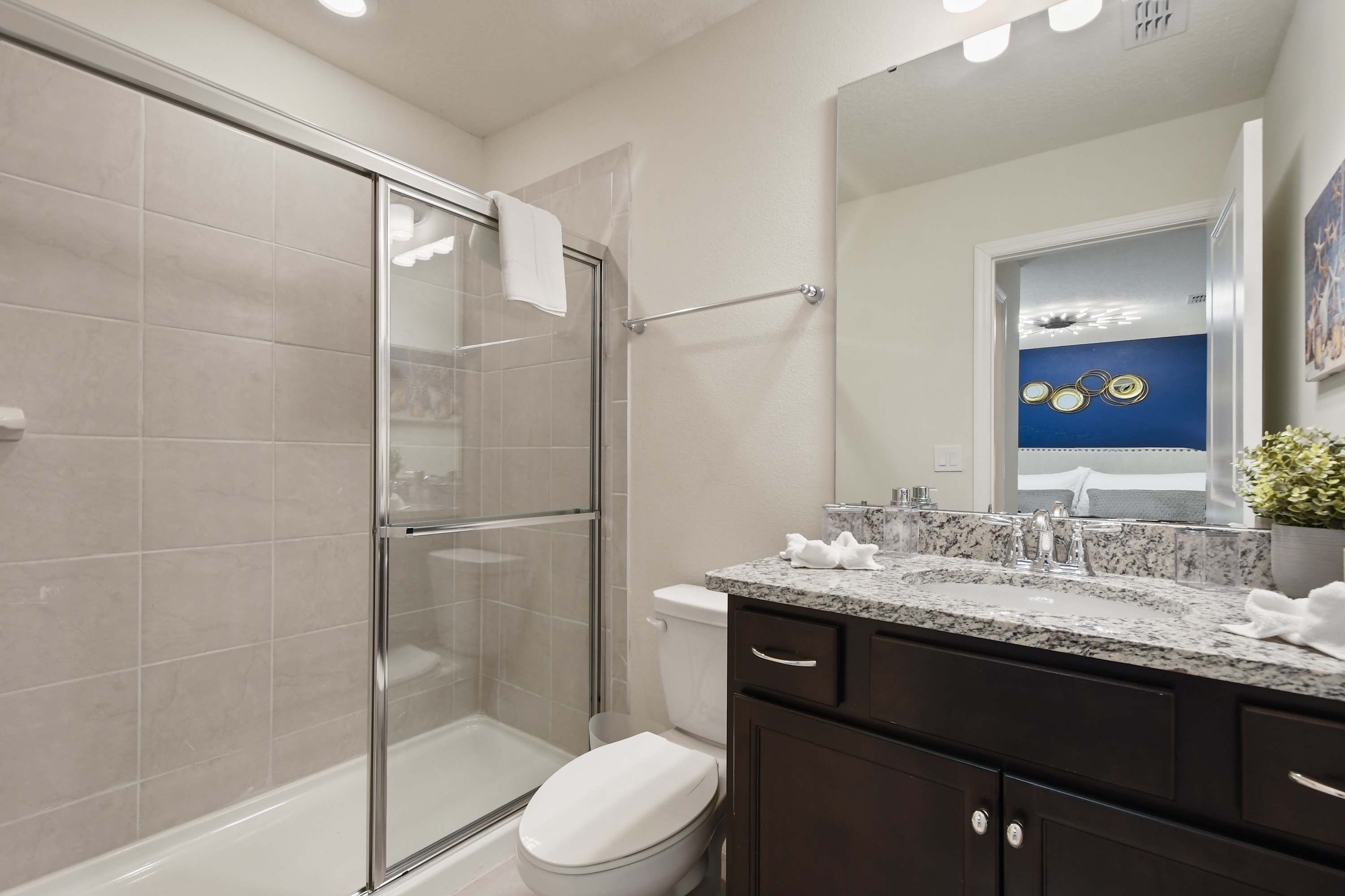 A modern bathroom with a glass shower enclosure, a white toilet, a granite countertop sink, and dark cabinetry.