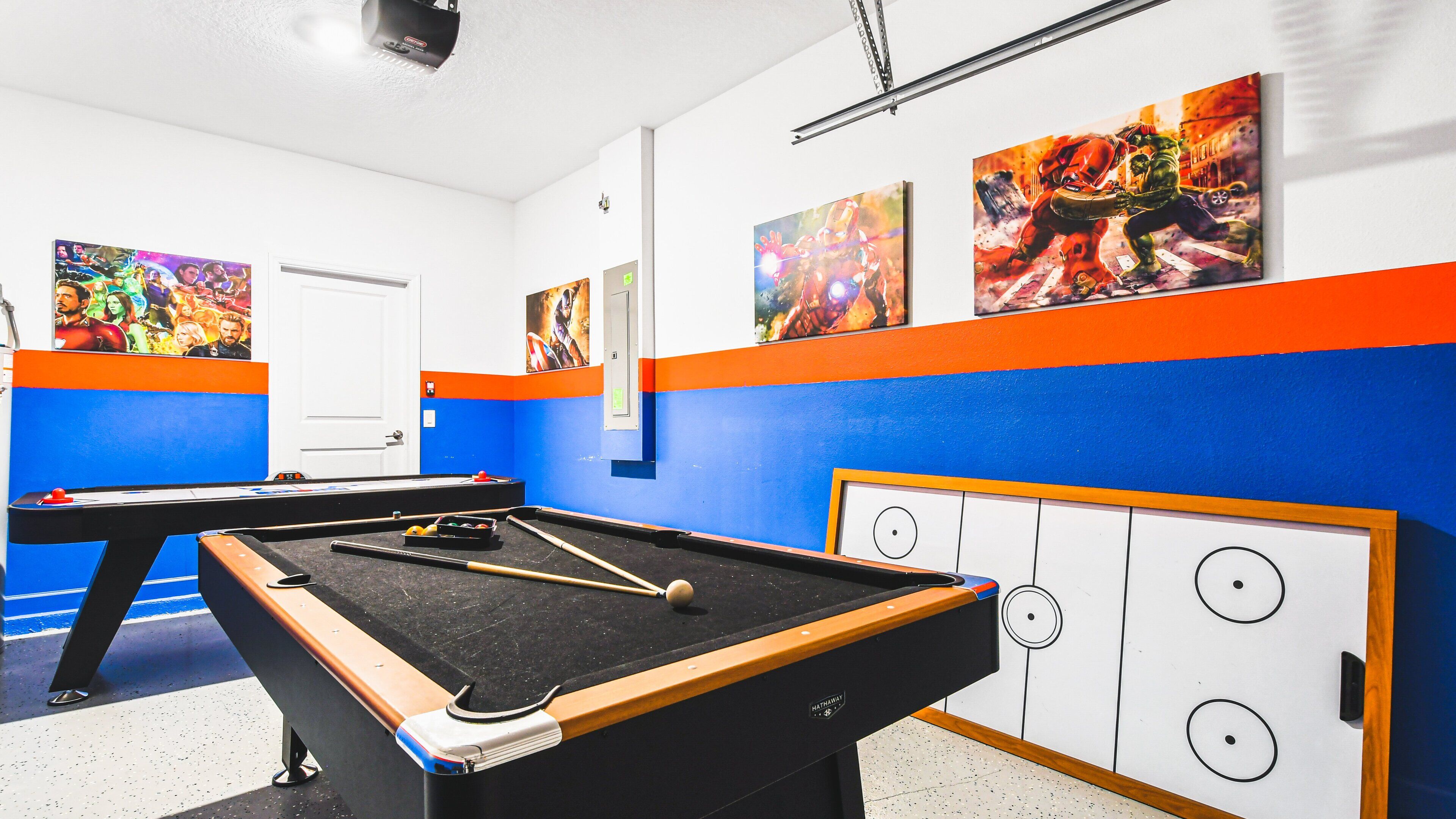 A pool table with a blue and orange wall, a billiards cue, and a pool ball.