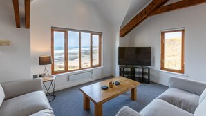 Een ruime woonkamer met grote ramen, een flatscreen televisie en een houten salontafel.