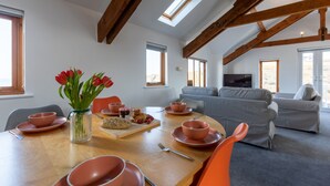 Een eetruimte met een houten tafel, oranje stoelen en roze servies. Op de tafel staat een vaas met rode bloemen.