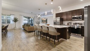 A modern kitchen with dark wooden cabinets, stainless steel appliances, and a central island with bar stools. - Veranda Palm Resort 12br Pool Spa Villa 2528 (Kissimmee)