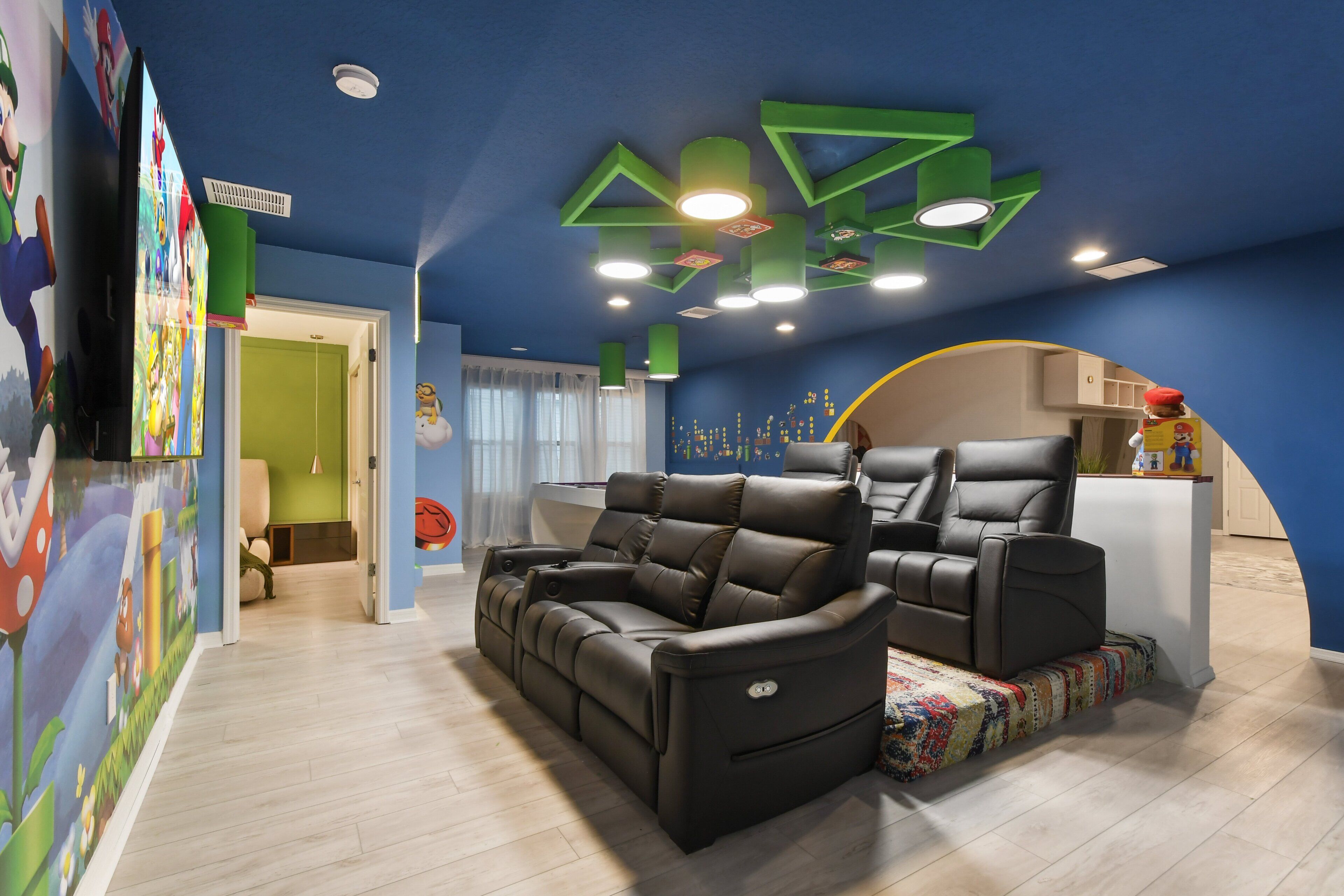 A living room with a black leather sofa and two recliners, a green ceiling design, and a wall with colorful cartoon characters.