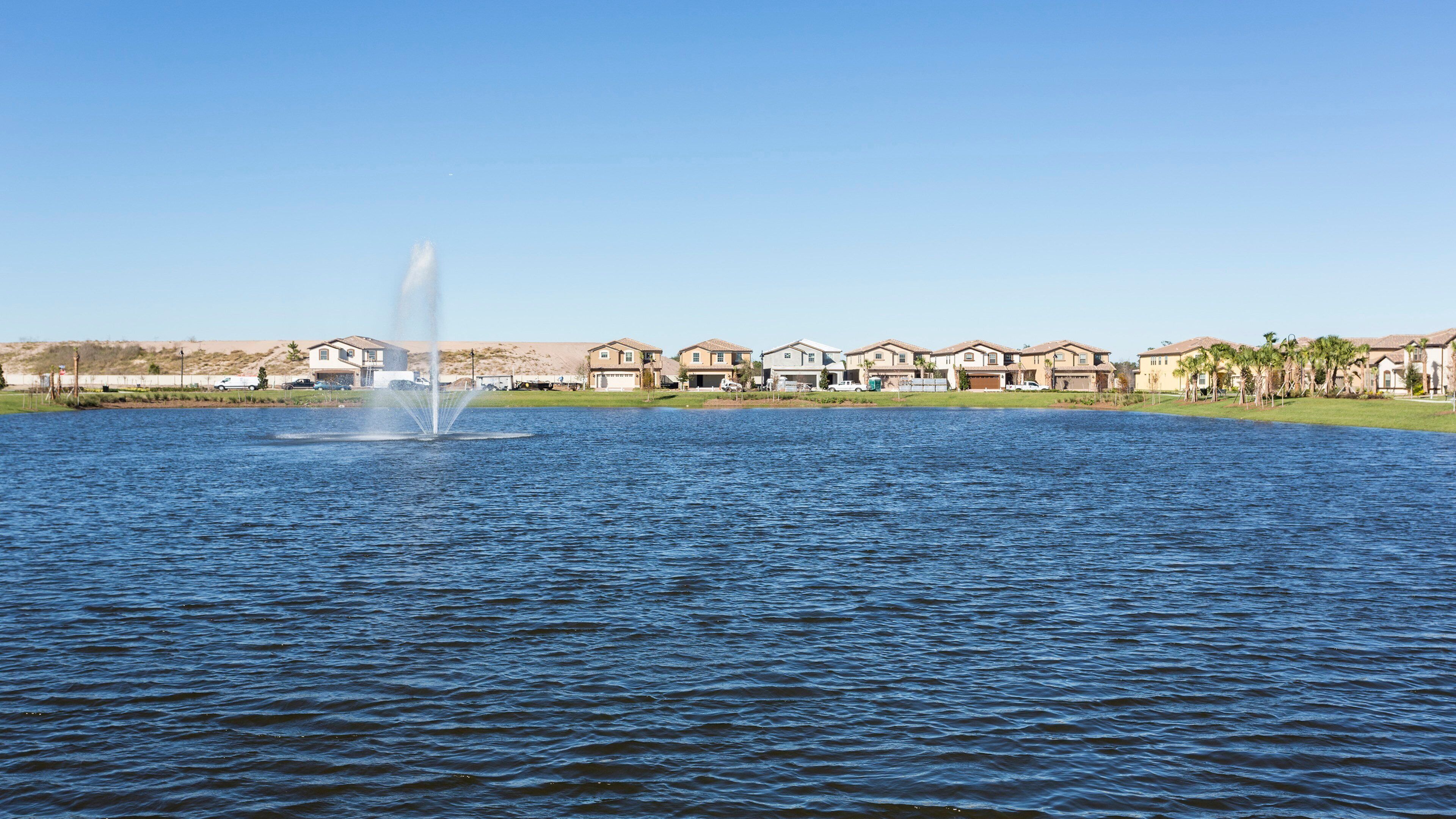 Een woongebied met huizen aan een meer, een fontein in het water en een heldere lucht.