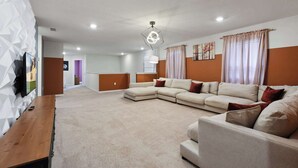 A modern living room with a sectional sofa, a wooden coffee table, and a flat-screen TV mounted on the wall. - 7BR Solterra Resort - Newly Renovated Home w Pool (Davenport)