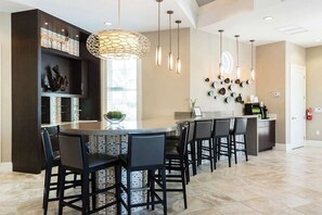 Cozinha moderna com ilha central, banquetas de bar, iluminação pendente e arte decorativa na parede.