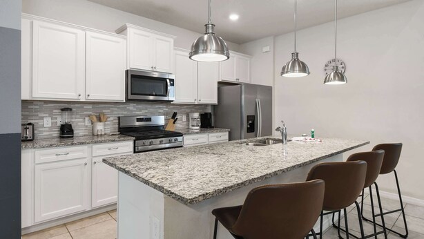 A modern kitchen with white cabinetry, stainless steel appliances, granite countertops, and pendant lighting. - 7BR Solterra Resort - Newly Renovated Home w Pool (Davenport)