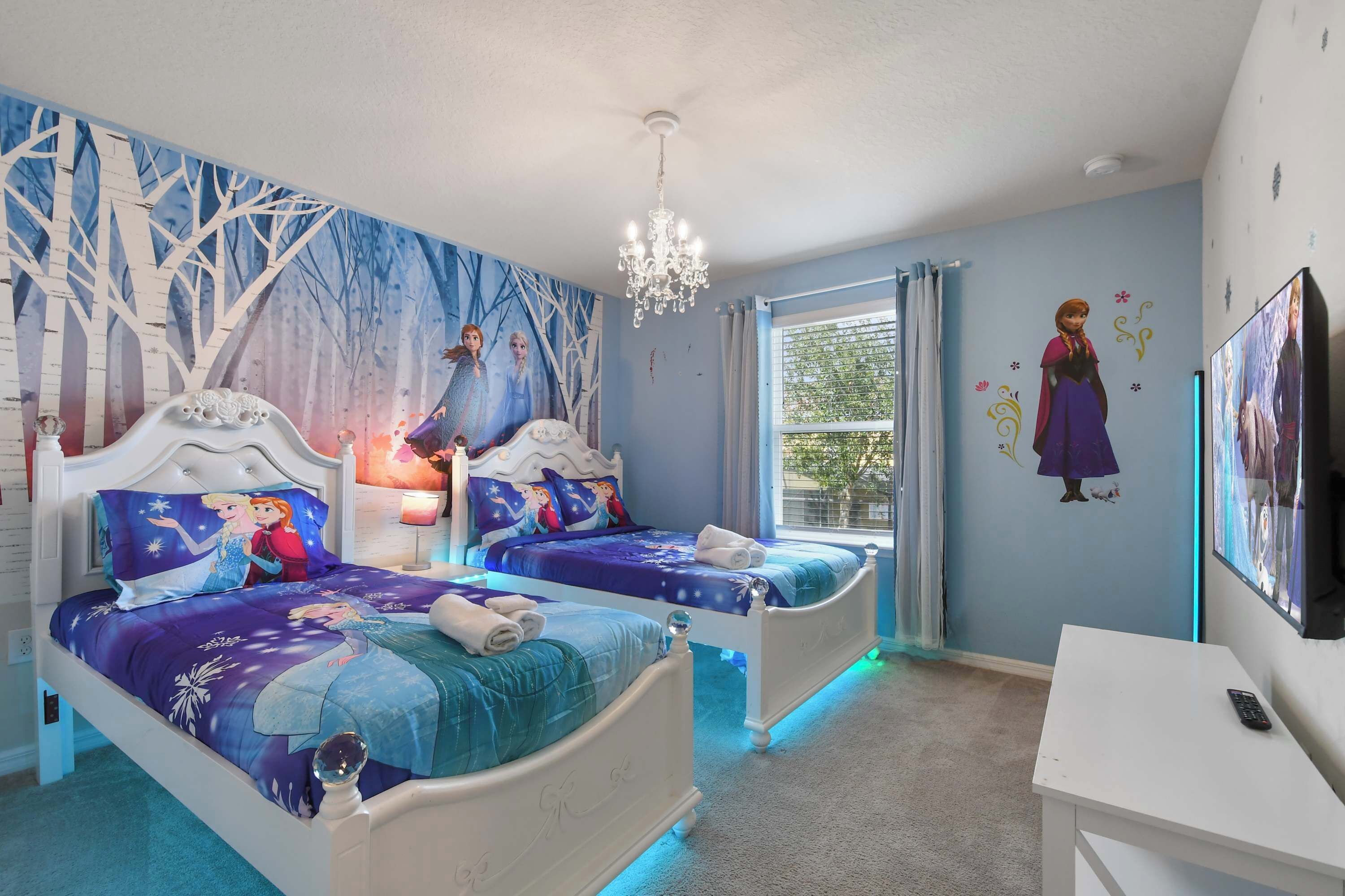 A bedroom with two beds, a chandelier, a TV, and a window with curtains.