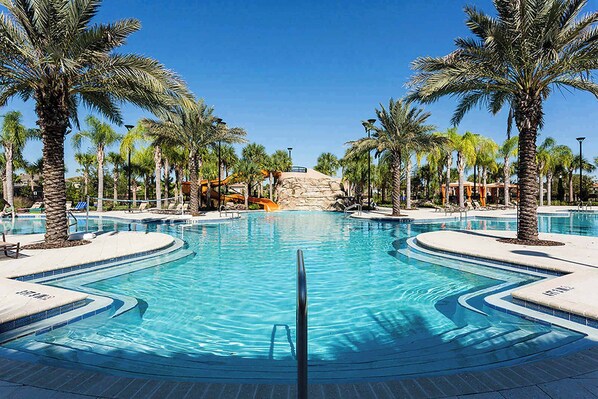 A large, clear swimming pool with palm trees and lounge chairs around it.