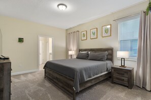 Een slaapkamer met een bed, nachtkastje, lamp en ingekaderde foto’s aan de muur.