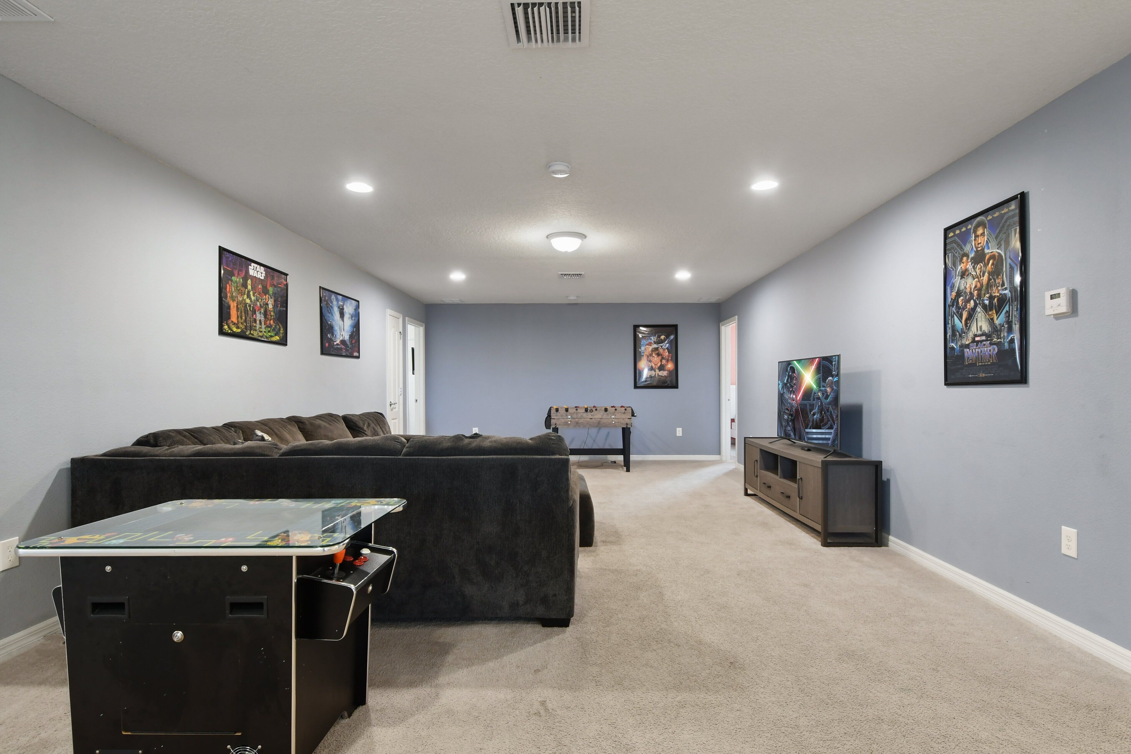 A living room with a sectional sofa, a foosball table, and a TV.