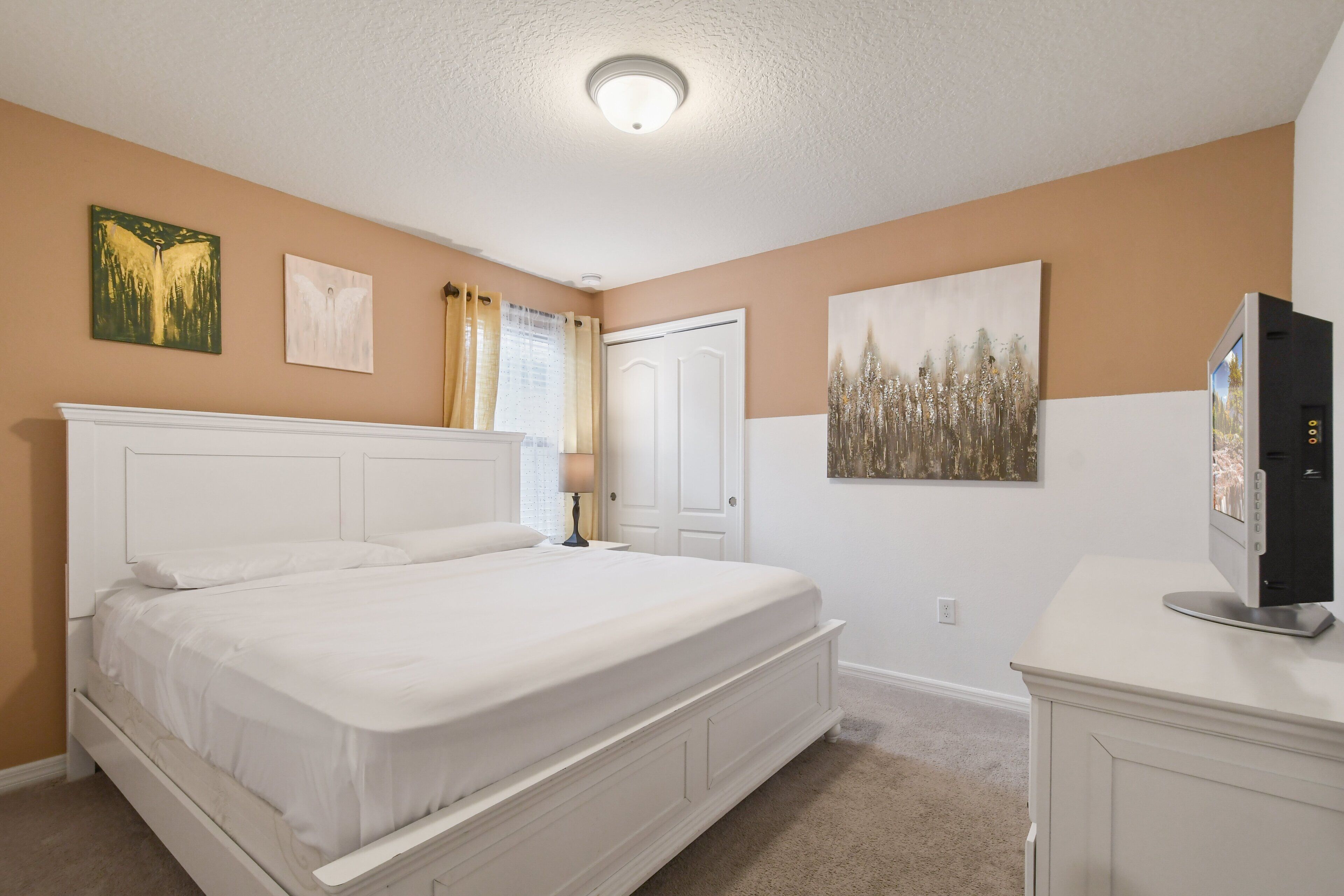A bedroom with a white bed, beige walls, and a ceiling light.