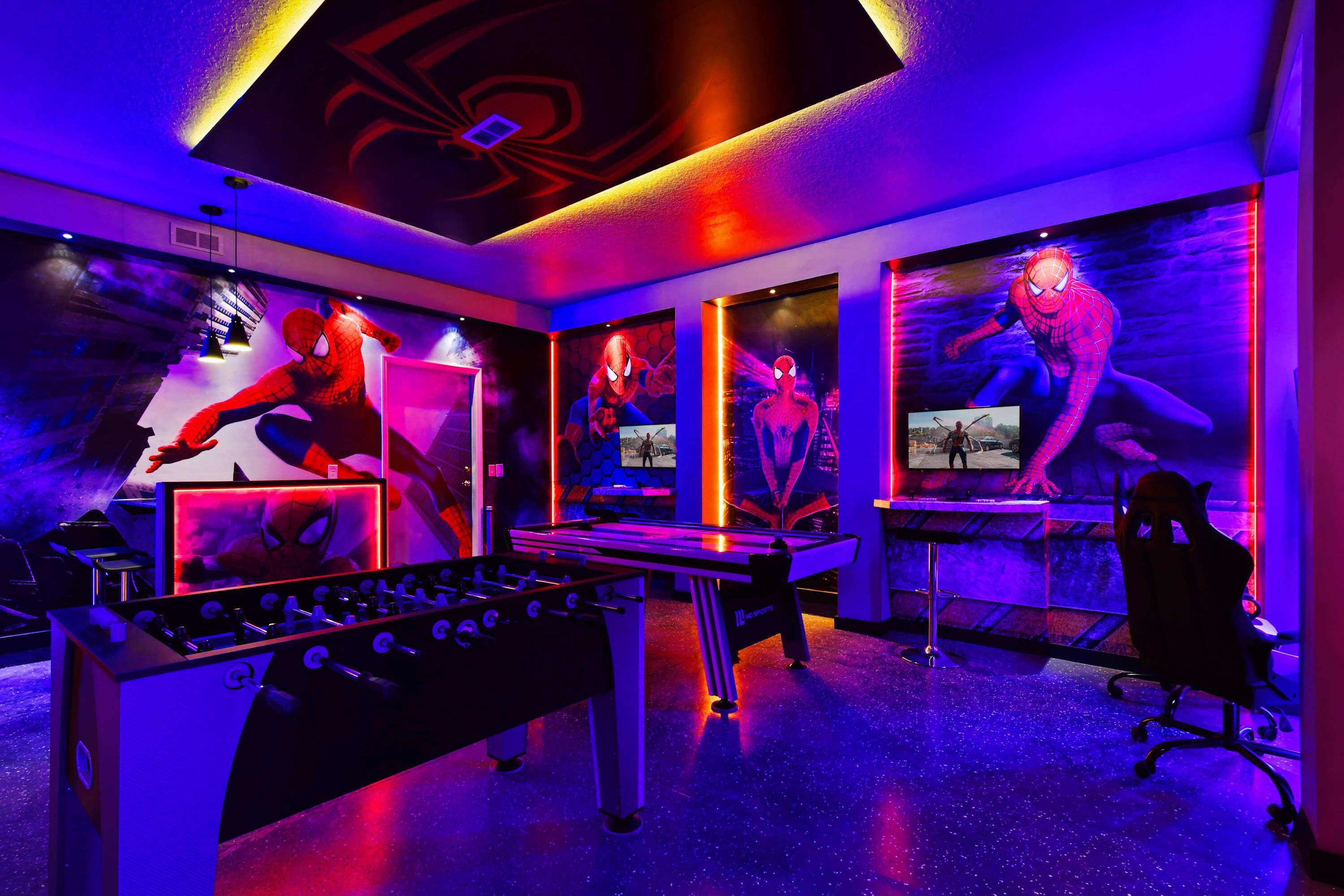 A room with a foosball table, a desk, and a chair. There are posters on the walls.