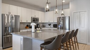 A modern kitchen with stainless steel appliances, a central island with bar stools, and pendant lighting. - Elegant Home With Pool & Spa, Close to Disney (Kissimmee)