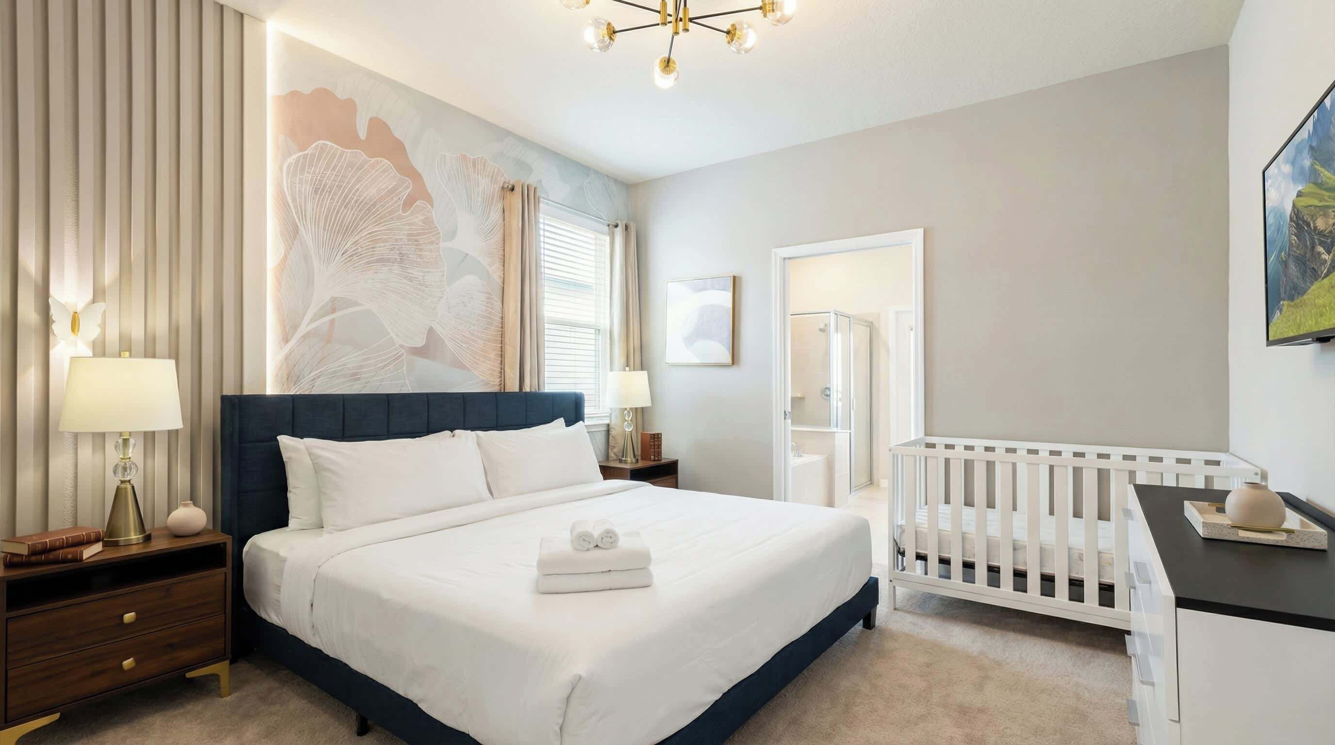 A hotel room with a large bed, a crib, a nightstand, a desk, and a wall with a large abstract painting.