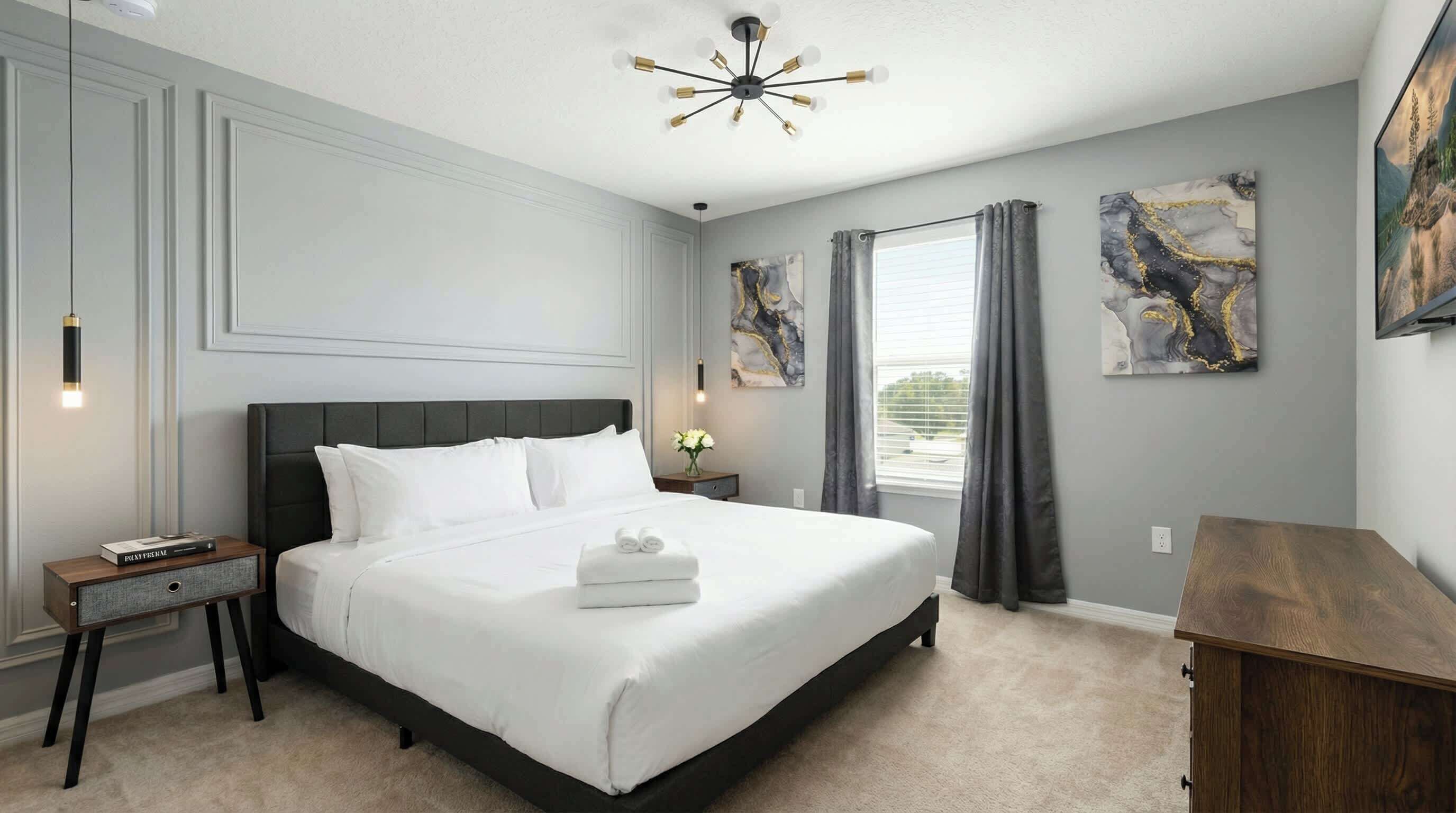 Une chambre à coucher bien aménagée, avec un grand lit, des tables de chevet, une petite table et une commode en bois.