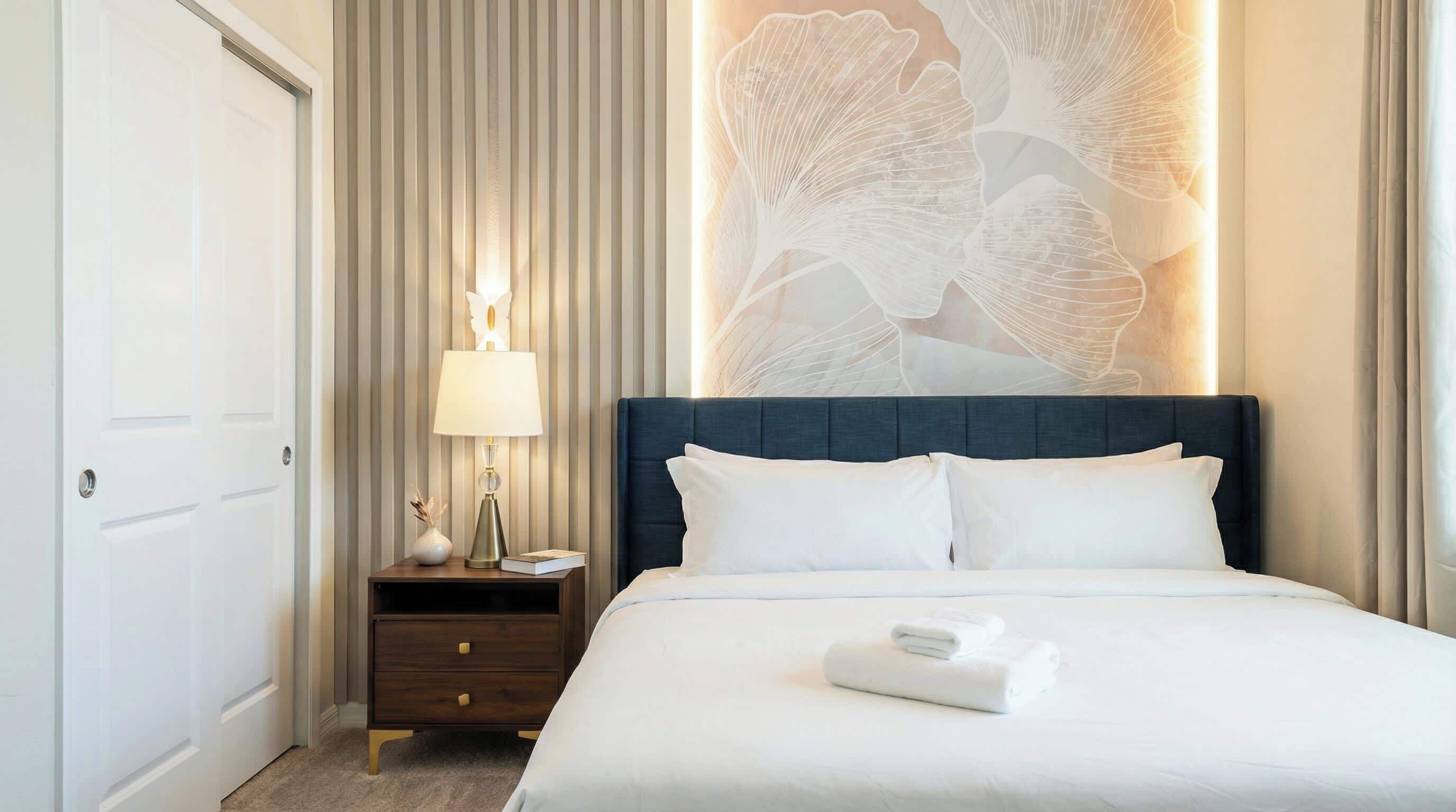 Une chambre d’hôtel avec un grand lit, une table de chevet avec une lampe et un mur orné d’un motif floral.