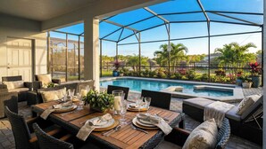 A covered outdoor dining area with a pool, wicker furniture, and a view of the pool and surrounding greenery. - Spacious Home w/ Private Pool, Near Disney (Davenport)