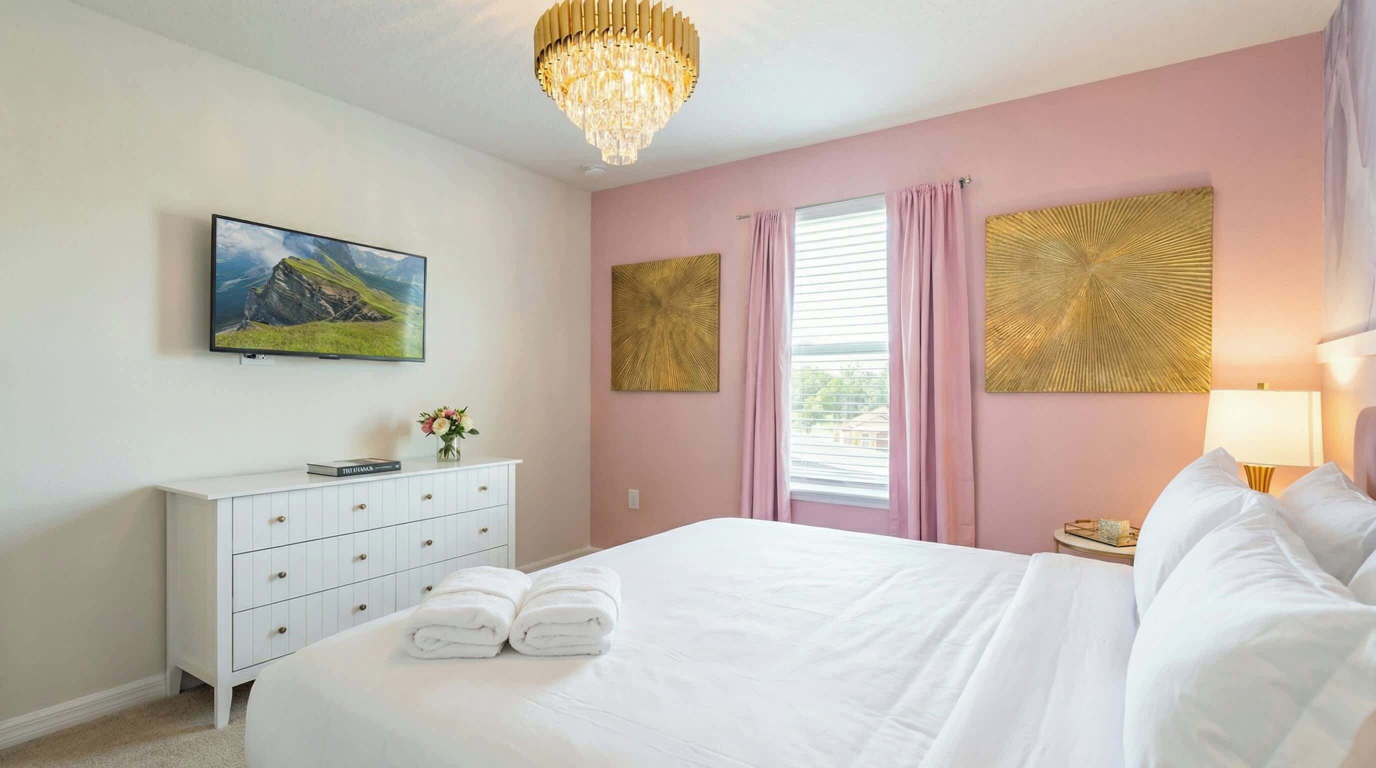 A bedroom with a bed, a dresser, a chandelier, and artwork on the walls.