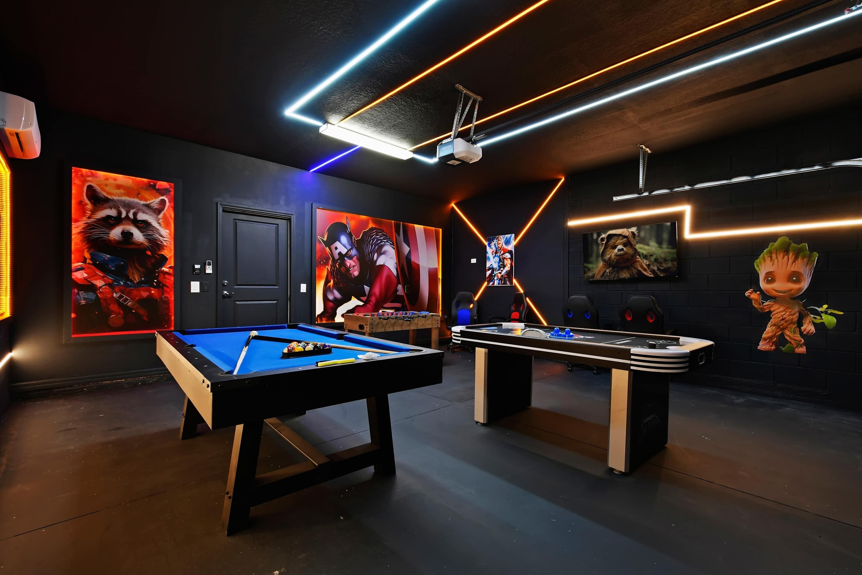 A room with a pool table, foosball table, and wall art featuring animated characters.