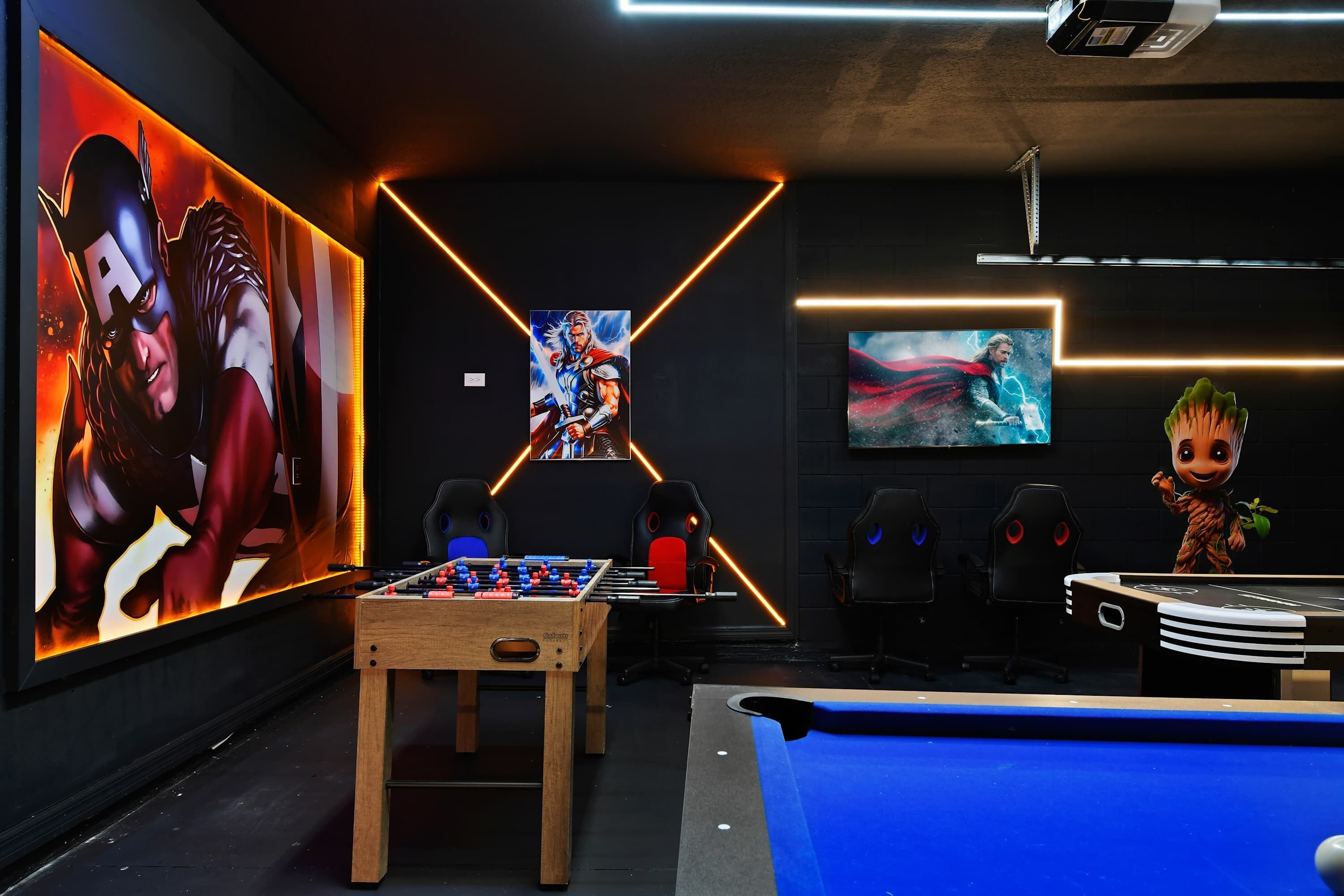 A modern gaming room with a foosball table, a pool table, and large wall art featuring superhero characters.