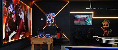 A modern gaming room with a foosball table, a pool table, and large wall art featuring superhero characters.