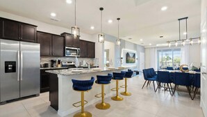 A modern kitchen with dark cabinets, stainless steel appliances, and a central island with bar stools. - Spacious Home w/ Private Pool, Near Disney (Davenport)