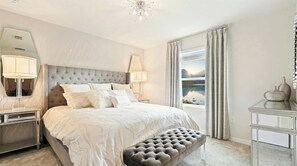 A bedroom with a large bed, bedside lamps, a tufted headboard, a bench, a dresser, and a window with a view of mountains. - Next to Clubhouse NEW Model Home Pool/spa/game/bbq (Davenport)