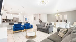 Uma sala de estar moderna com um sofá cinza, poltronas azuis e uma mesa de centro de vidro.