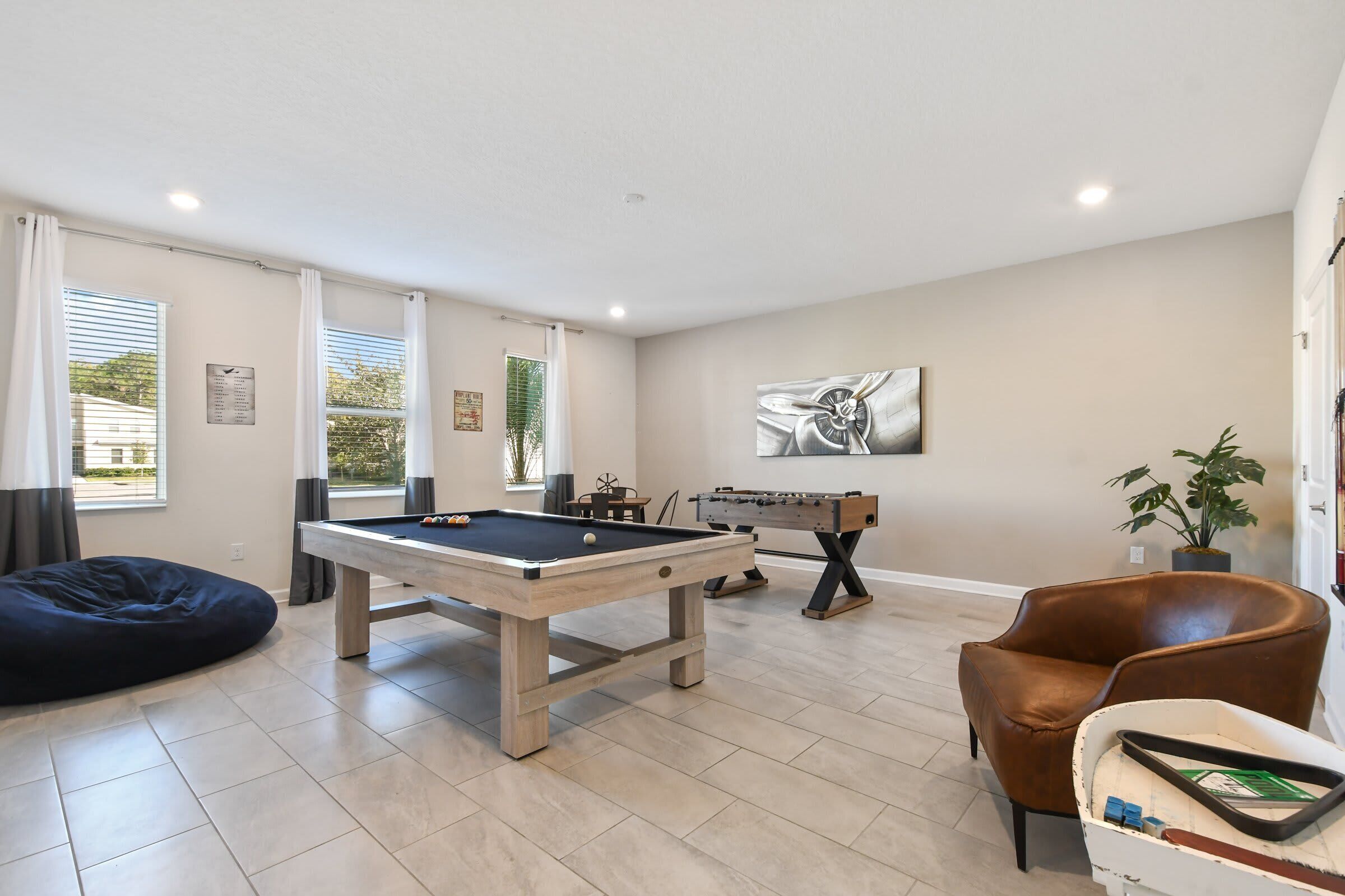 A living room with a pool table, a foosball table, a brown leather chair, and a potted plant.