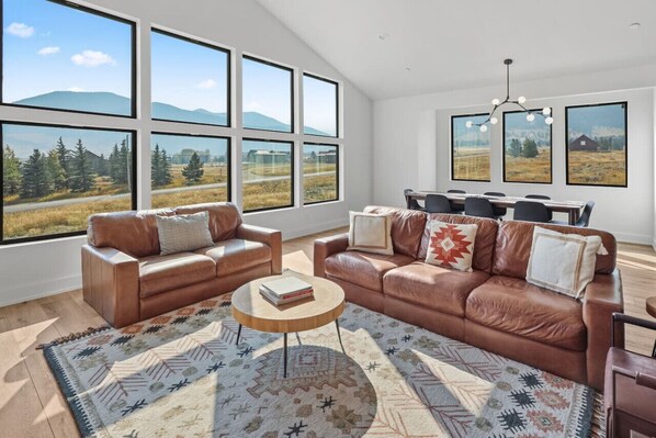 A spacious living room with leather sofas, a round coffee table, and large windows offering a view of a mountainous landscape.
