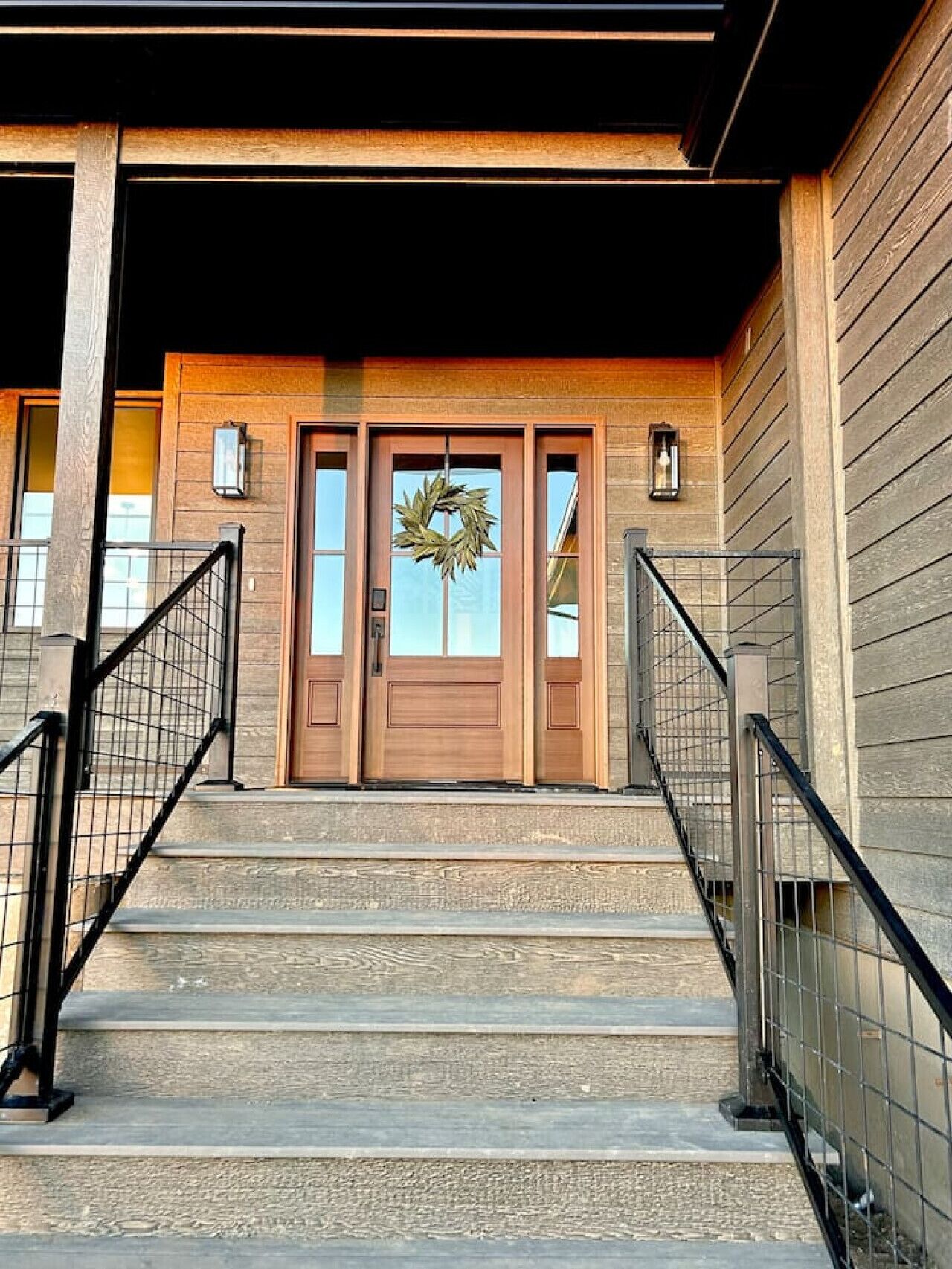 A wooden building with a front door, two windows, and a staircase with metal railings.