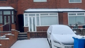 A residential building with a garage, a covered car, and a blue trash bin. - Charming 2-bedroom Home With Modern Amenities (Oldham)