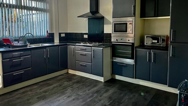 A modern kitchen with dark cabinetry, a built-in oven, microwave, and a gas stove. - Charming 2-bedroom Home With Modern Amenities (Oldham)