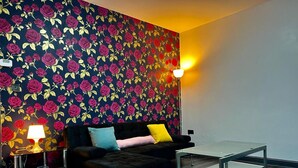 A modern living room with a dark-colored sofa, a glass coffee table, and a patterned wallpaper. - Charming 2-bedroom Home With Modern Amenities (Oldham)