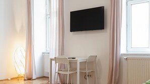 Une pièce avec une table et des chaises blanches, un téléviseur à écran plat accroché au mur et un radiateur.