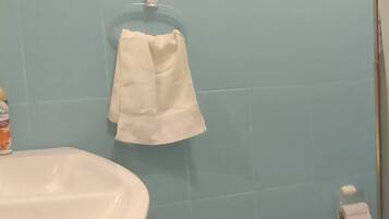 A bathroom with a white sink, blue tiled walls, a white towel hanging on a rack, and a toilet with a paper towel holder.