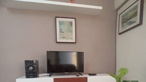 Un salon avec un téléviseur à écran plat posé sur un meuble blanc, un buffet en bois en dessous, un tapis à motifs et une plante en pot sur une table.