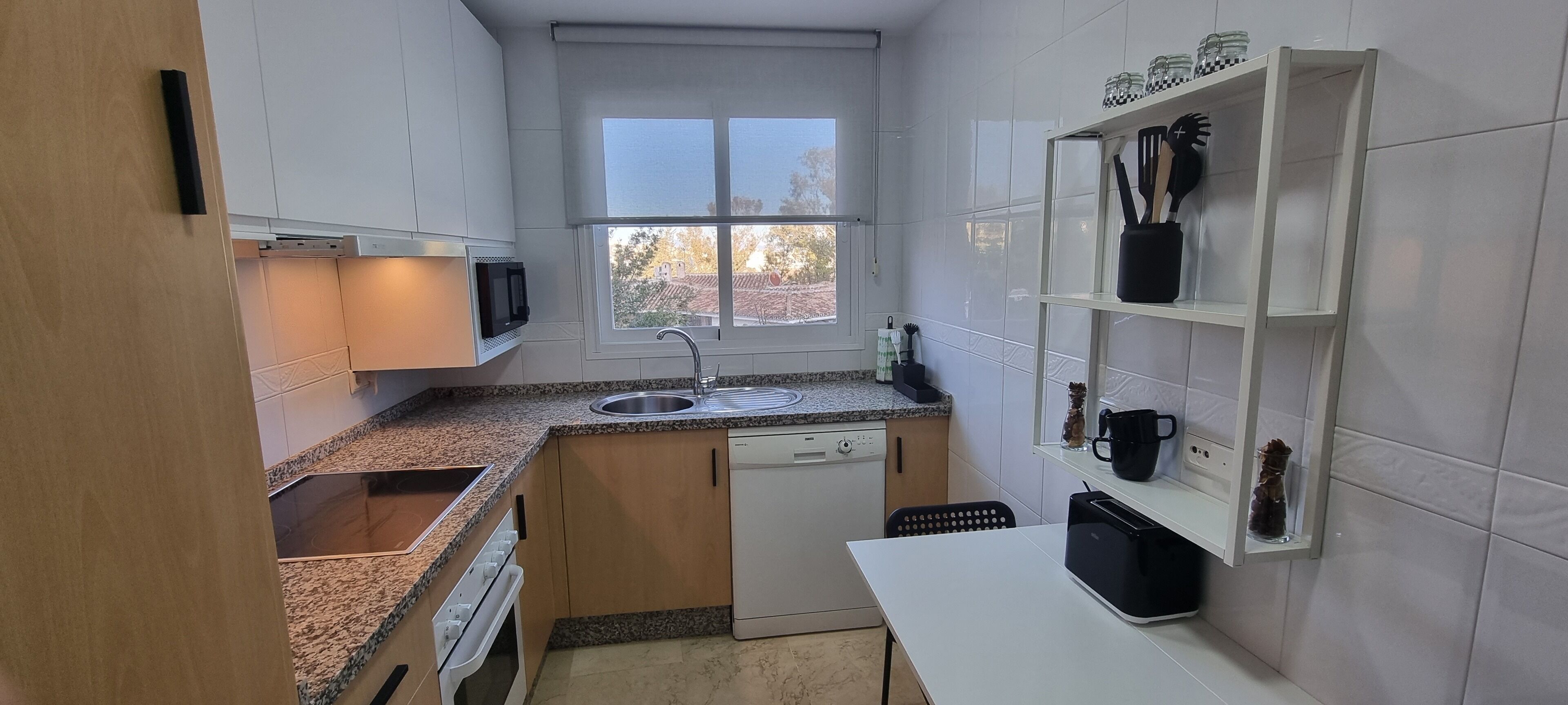 Cozinha compacta com lava-louças, micro-ondas e janela que traz luz natural.