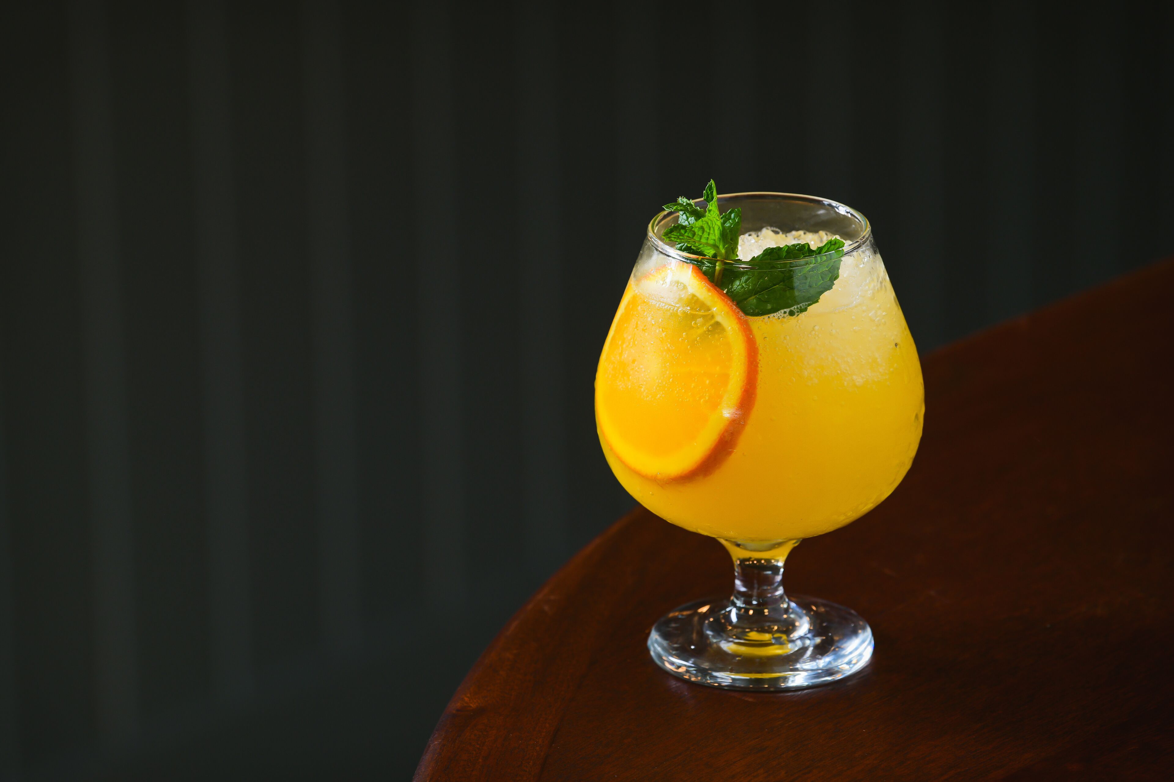 Un vaso de jugo de naranja con una rodaja de naranja y hojas de menta sobre una mesa de madera.
