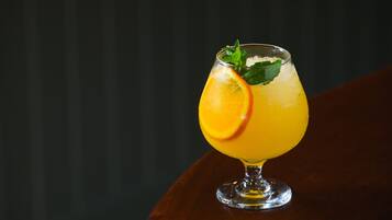 Un vaso de jugo de naranja con una rodaja de naranja y hojas de menta sobre una mesa de madera.