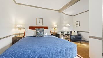 A spacious bedroom with a large bed, two bedside tables with lamps, a small side table, a chair, and a framed picture on the wall.