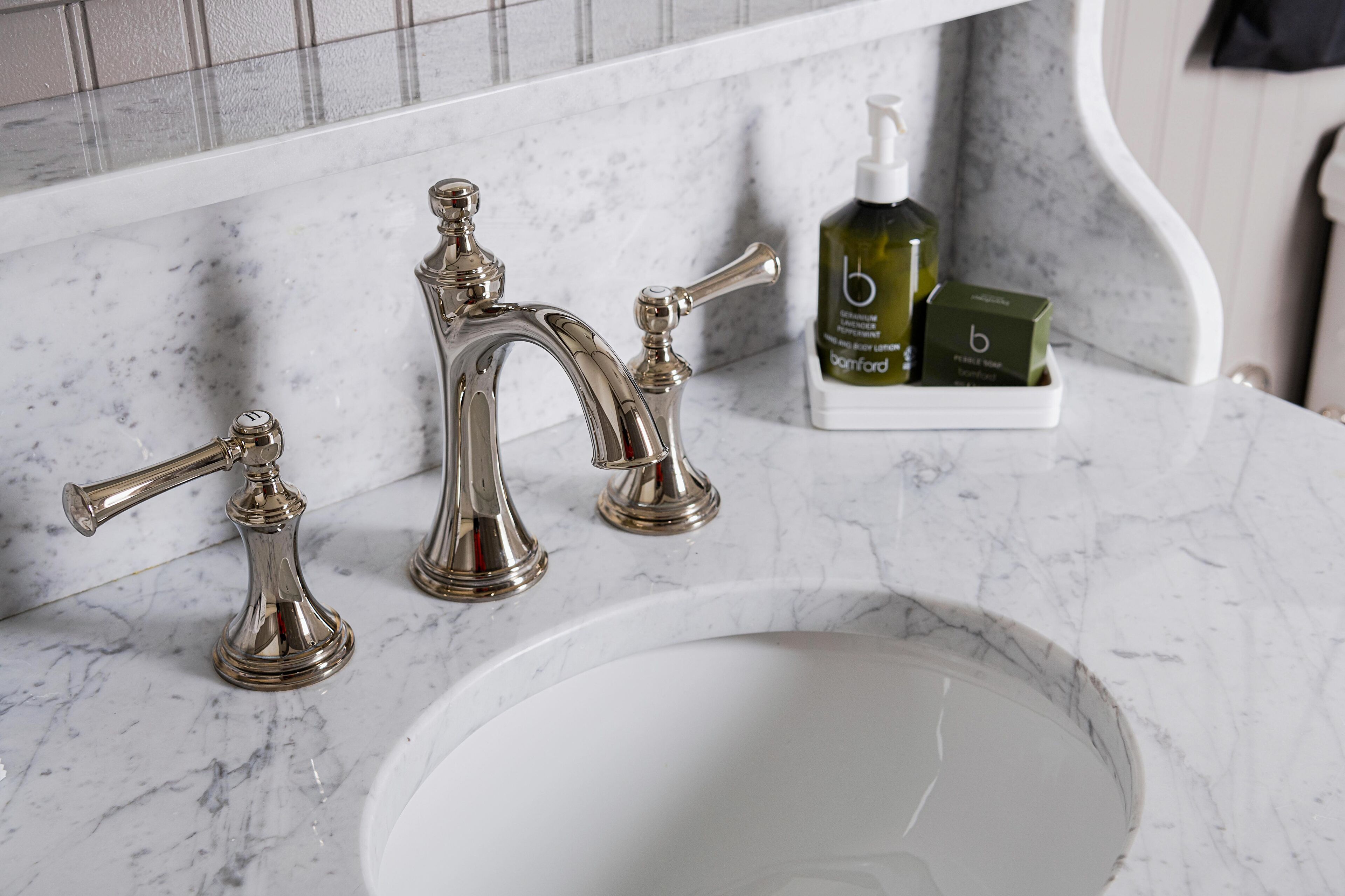 A bathroom with a marble sink, two chrome faucets, and a bottle of hand soap on the counter.