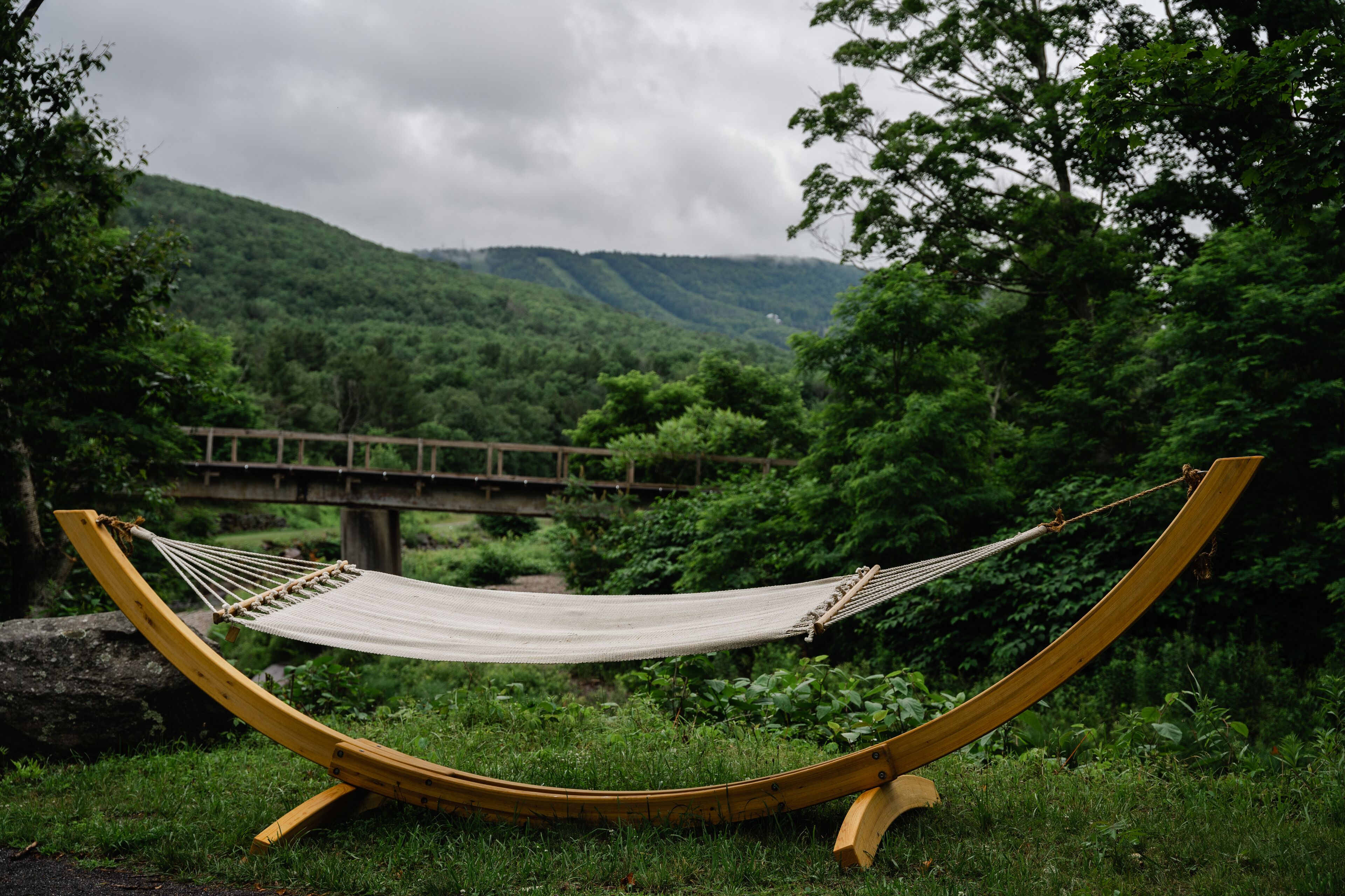 A hammock in a lush green setting with a bridge in the background.